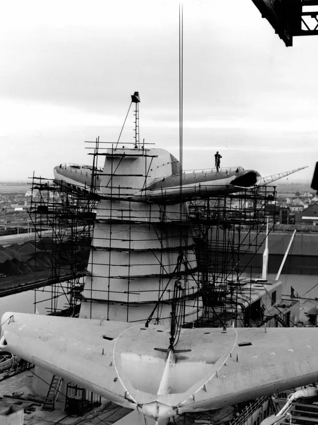 Dans le quai d'armement du bassin de Penhoët à Saint-Nazaire, des ouvriers des Chantiers de l’Atlantique procèdent à l'embarquement d'un aileron de cheminée du paquebot France (1962).